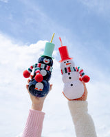 Hands holding Penguin and Snowman Sipper in air against sky background. 