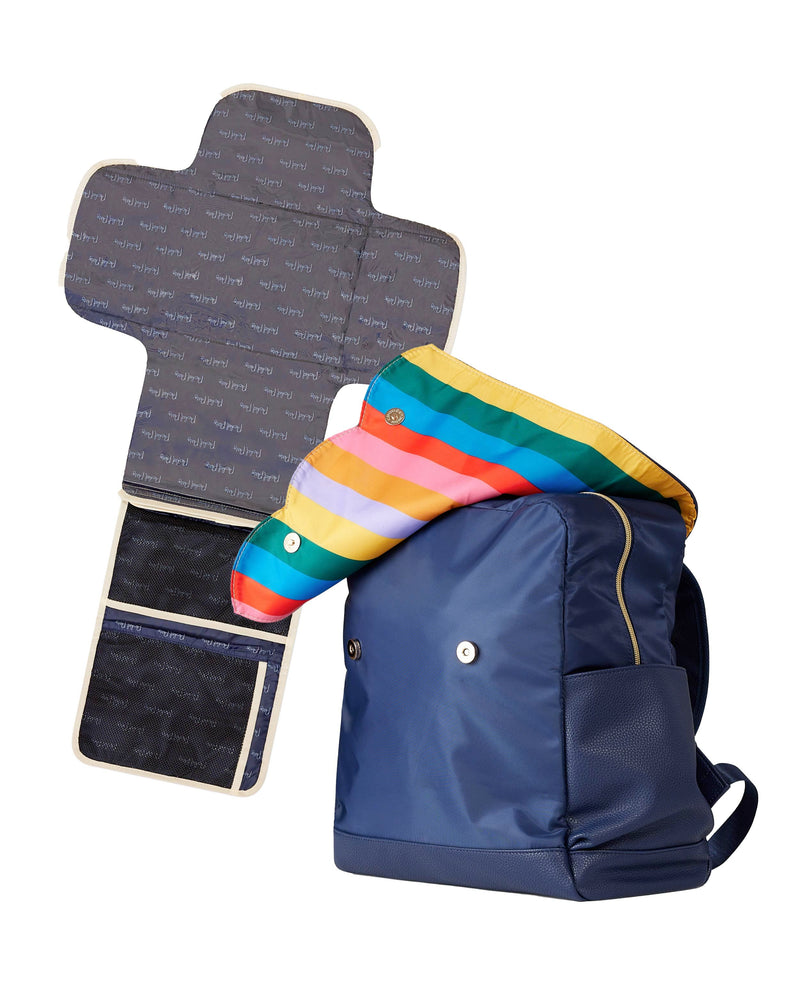 Navy diaper bag backpack with rainbow stripe lining next to portable changing pad