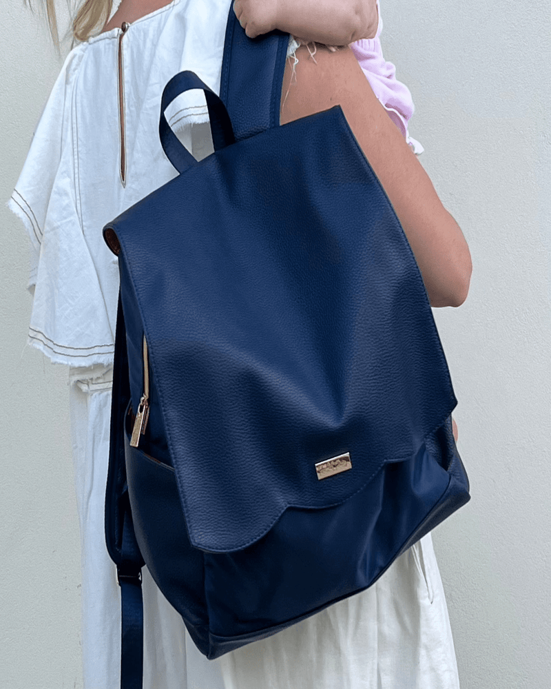 woman wearing navy diaper bag backpack on one shoulder holding baby