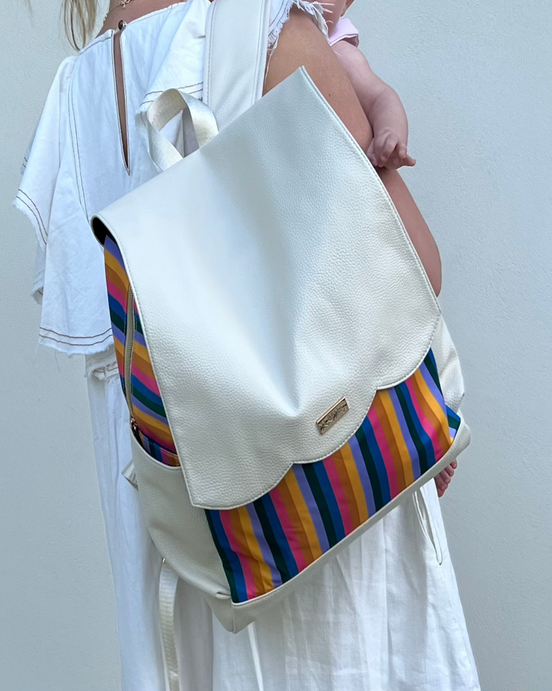 Woman holding baby and wearing diaper bag backpack with rainbow stripes on one shoulder