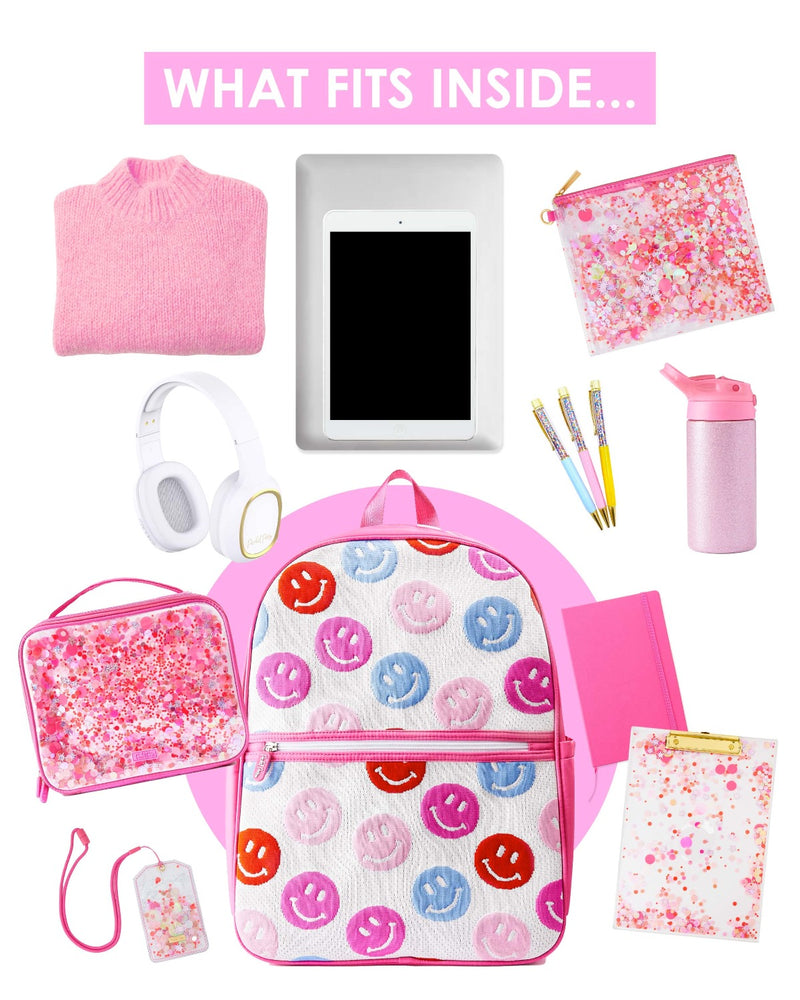 Text on top of the image reads, "What fits inside." Items are displayed across a white background surrounding a pink and white knit backpack with blue, pink, purple and red smiley faces. The items include: a pink sweater, pink everything pouch, confetti pens, white headphones, a pink glitter water bottle, a pink confetti lunchbox, a pink clipboard, a pink note book, a pink lanyard and a computer and tablet.