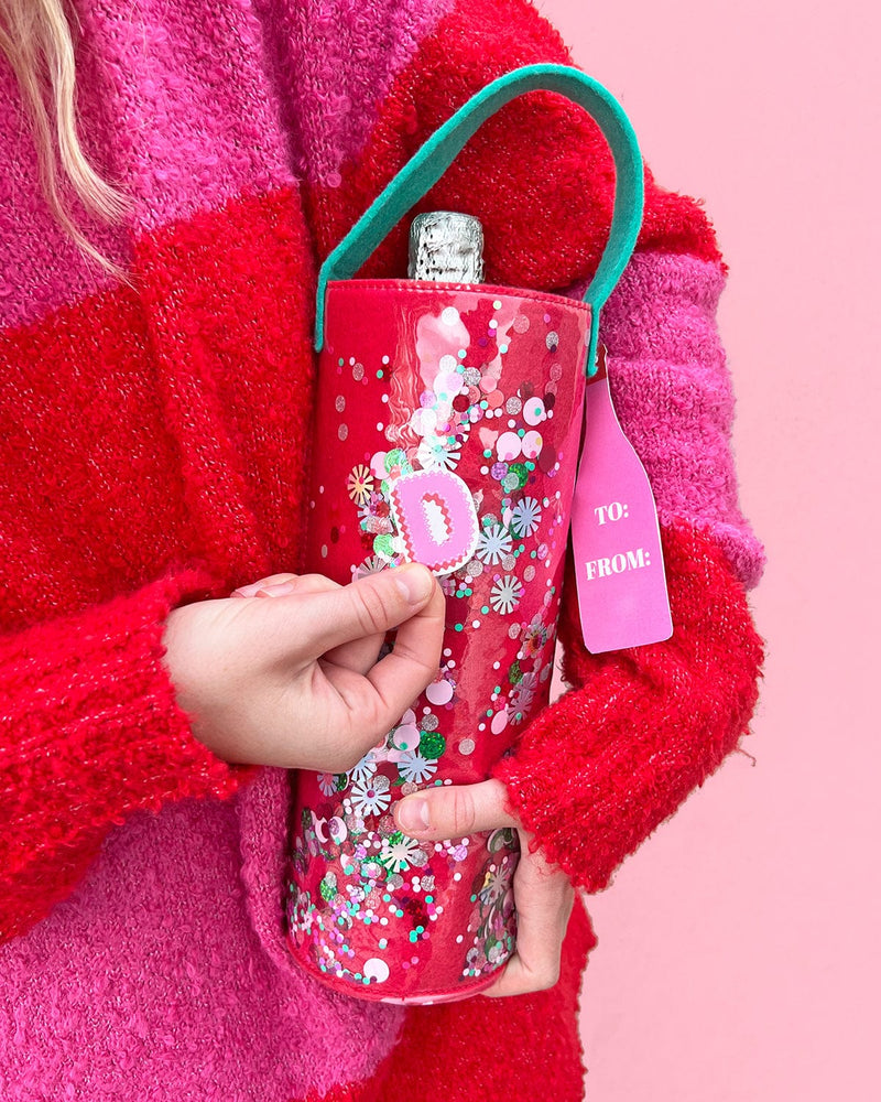 Hand placing Alphabet Vinyl Sticker on confetti wine bag shot against pink background. 