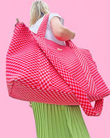 Large pink and red checkered bag on woman's shoulders against pink background