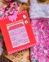 Holiday Puzzle packaging placed with pink confetti Santa hat and stocking.