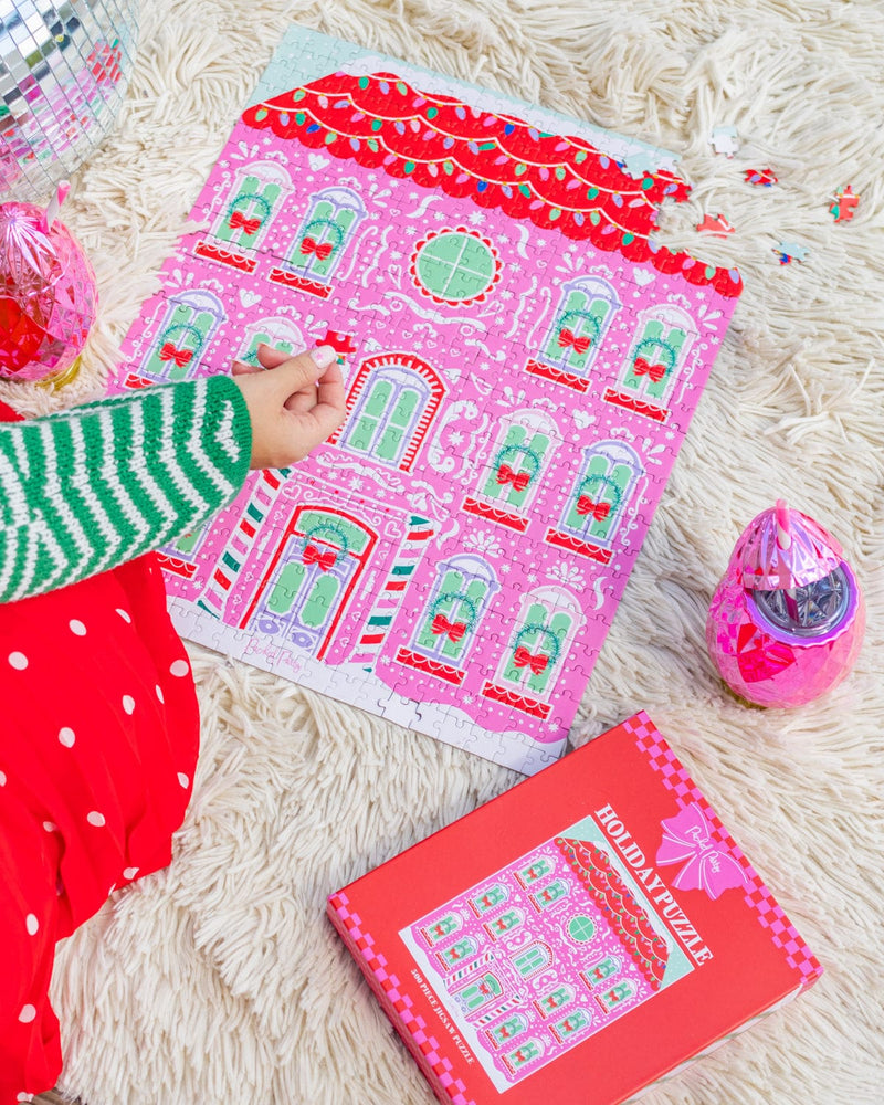 Hand placing piece into gingerbread house puzzle shot against white fur background. 