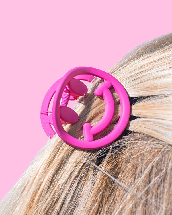 Pink smiley claw clip placed into hair shot against pink background. 