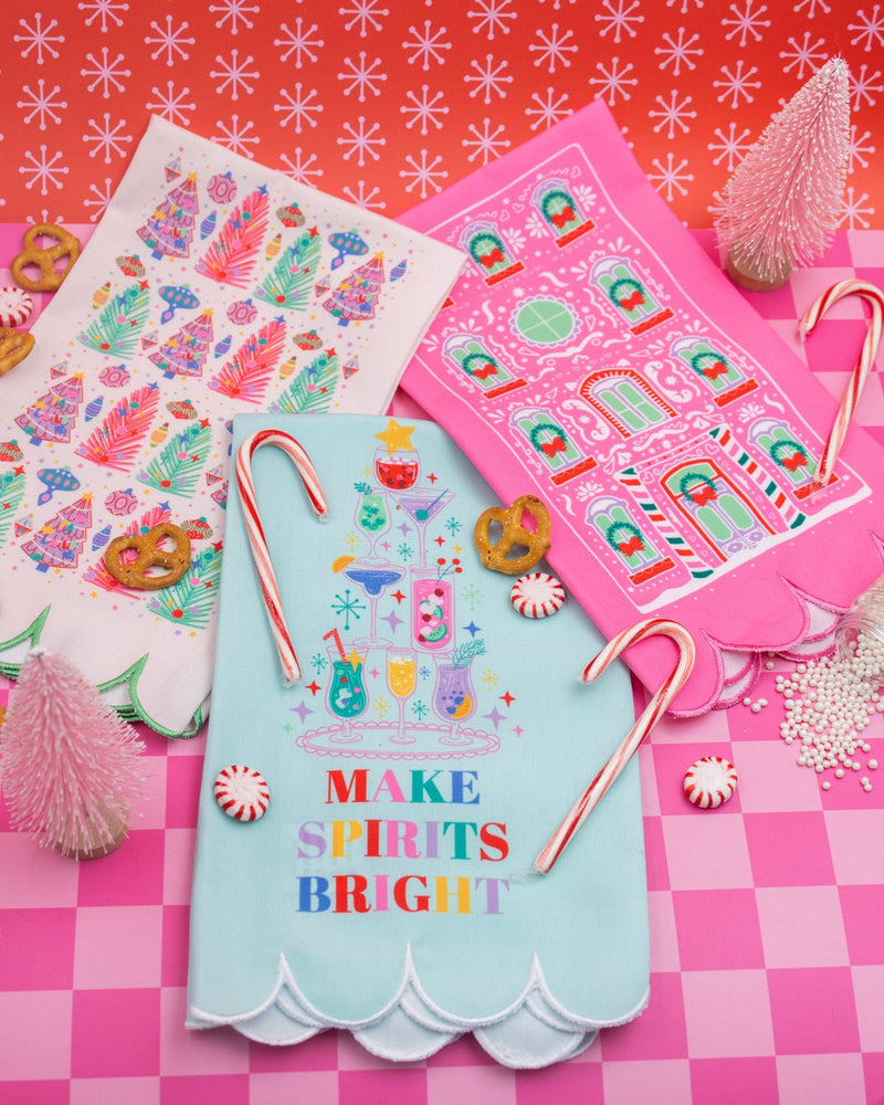 Light Blue 'Make Spirits Bright' tea towel with assortment of white and pink tea towels and holiday treats shot against pink checkered background. 