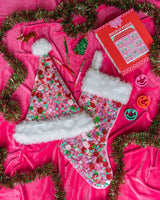 Pink confetti santa hat and pink confetti stocking surrounded by assortment of holiday products shot against hot pink background. 