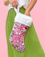 Woman holding pink confetti stocking with faux fur trim against pink background. 