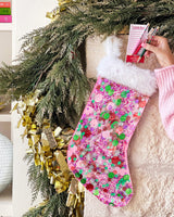 Hand placing items into pink confetti stocked placed on mantle with surrounding greenery. 