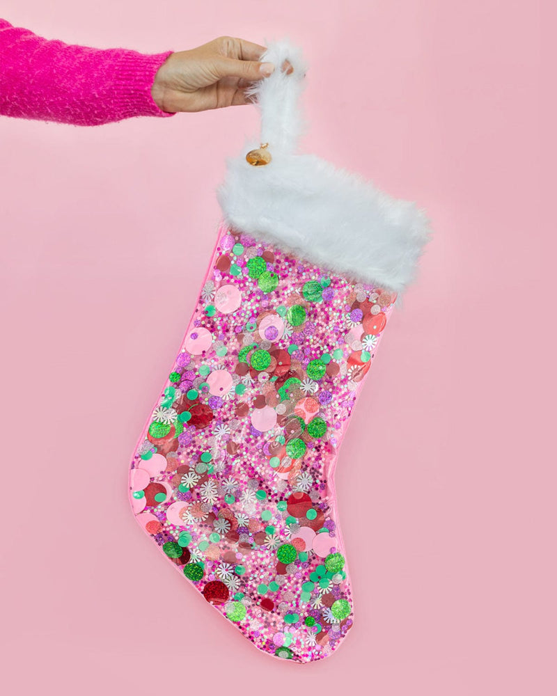 Hand holding pink confetti stocking with faux fur trim in the air shot against pink background. 