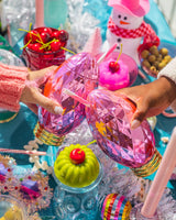 two girls reaching in to cheers over a holiday party tabletop display. they are holding vintage pink light sippers and the colors are very bright and beautiful