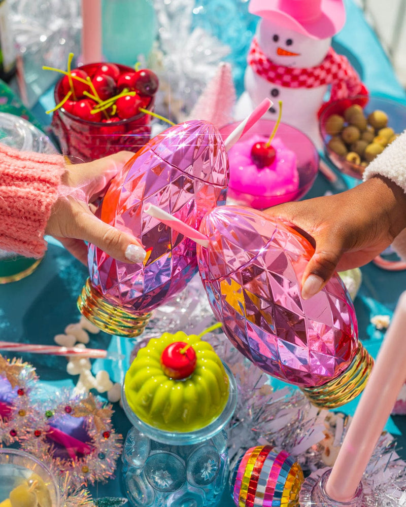 two girls reaching in to cheers over a holiday party tabletop display. they are holding vintage pink light sippers and the colors are very bright and beautiful