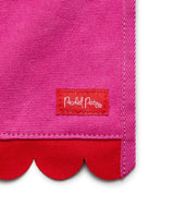 Close up of pink fabric, red scalloped edge, and red tag with 'Packed Party' logo shot against white background. 