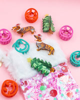 Assortment of holiday claw clips placed on pink confetti stocking shot against pink background. 