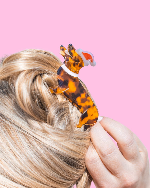 Santa dog claw clip placed in hair shot against pink background. 