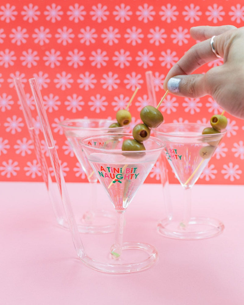 Hands putting olives into the 'A Tini Bit Naughty' martini glasses shot against patterned wallpaper. 