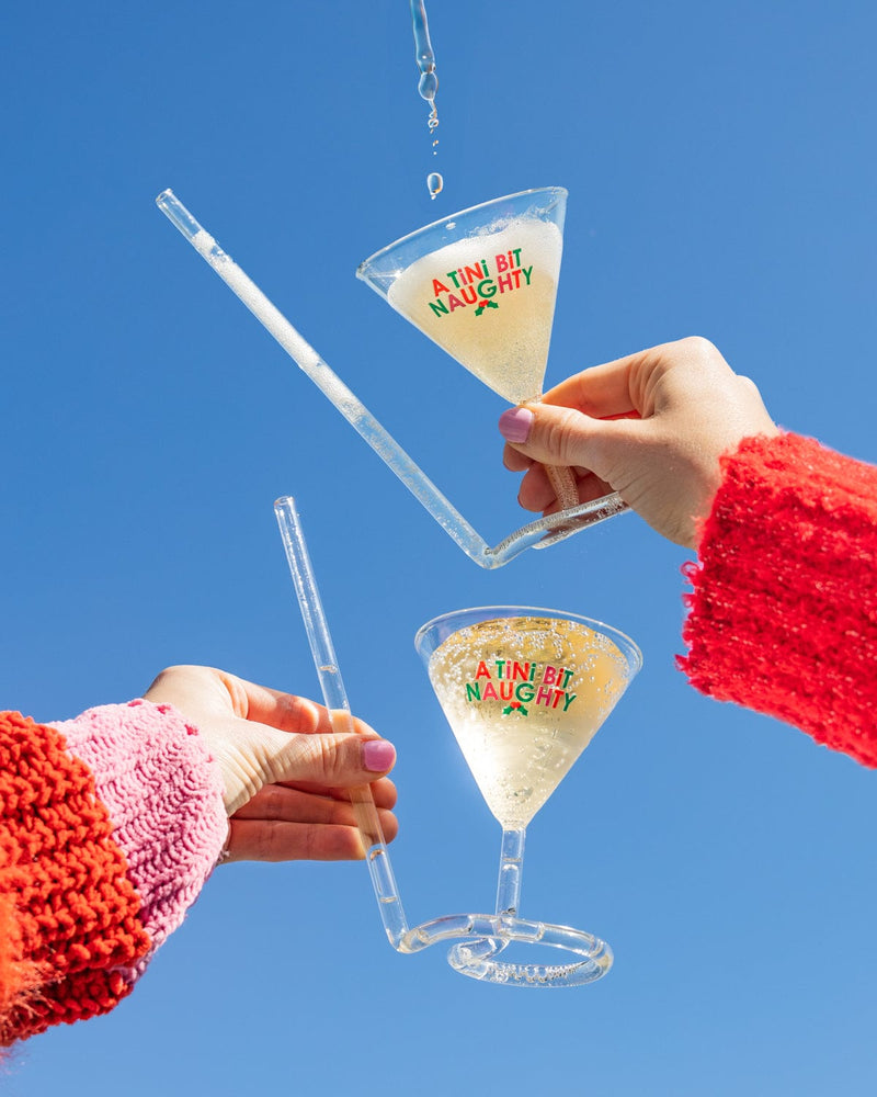 Hands holding 'A Tini Bit Naughty' martini glasses in air with liquid in them shot against the sky. 