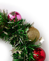 Close up of tinsel and ornament details on wreath headband shot against white background. 