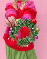 Woman holding wreath headband out shot against pink background. 