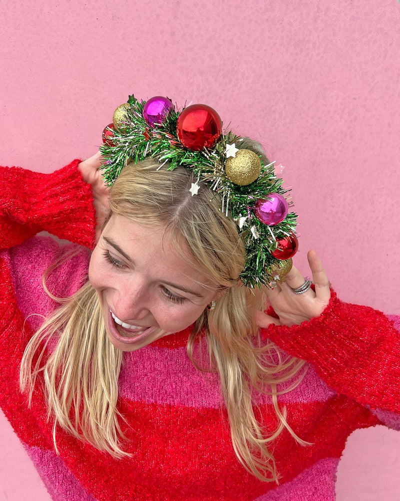 Smiling woman wearing wreath headband shot against pink background. 