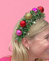 Close up sideview of woman wearing wreath headband shot against pink background. 