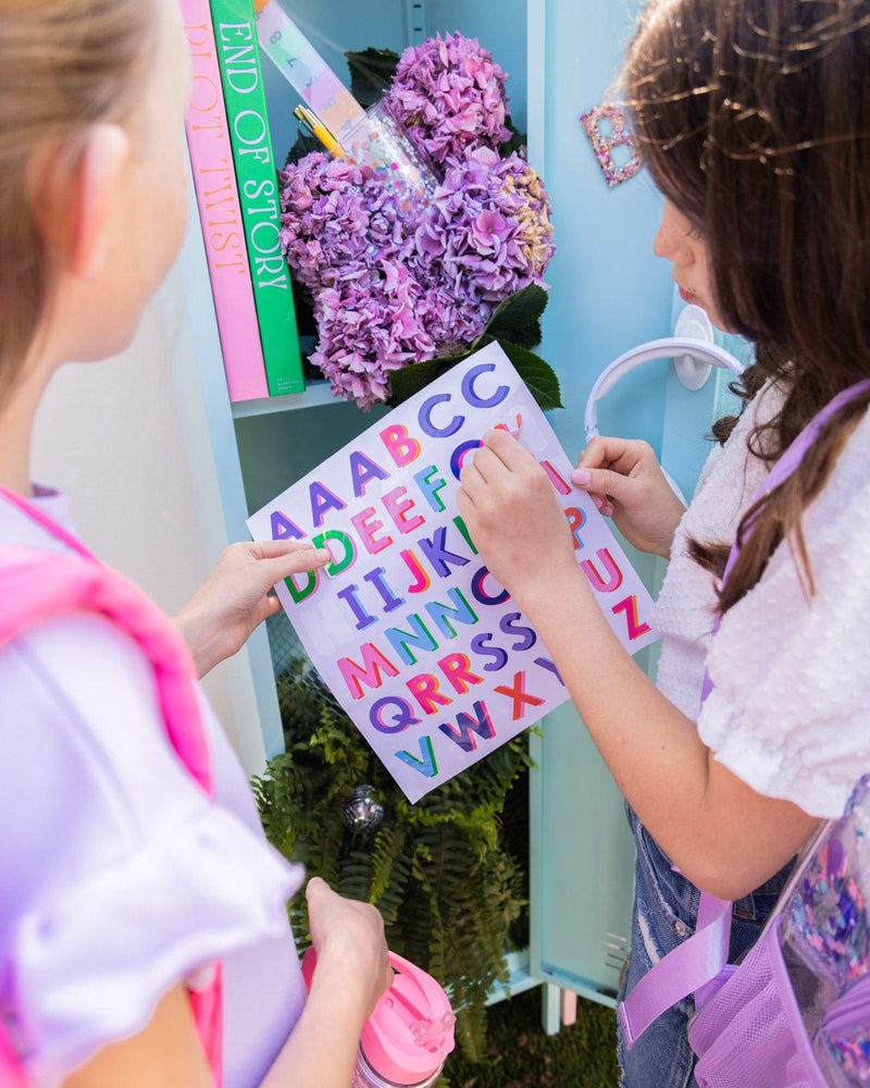 Two girls peel off stickers from the multi-colored  alphabet sticker sheet.