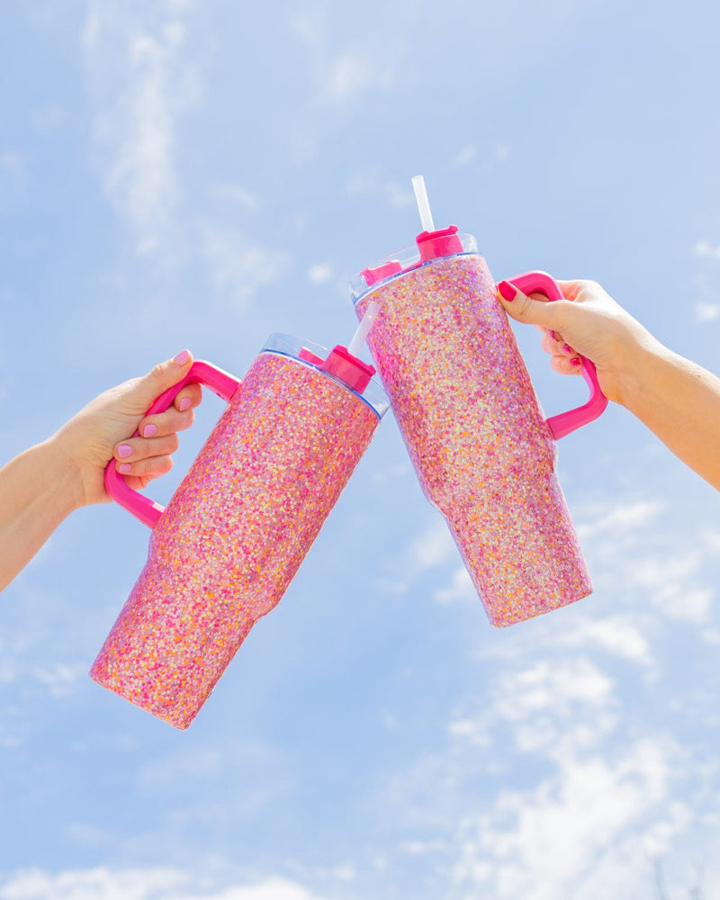 Two people hold up pink glitter tumblers up to the sky. 
