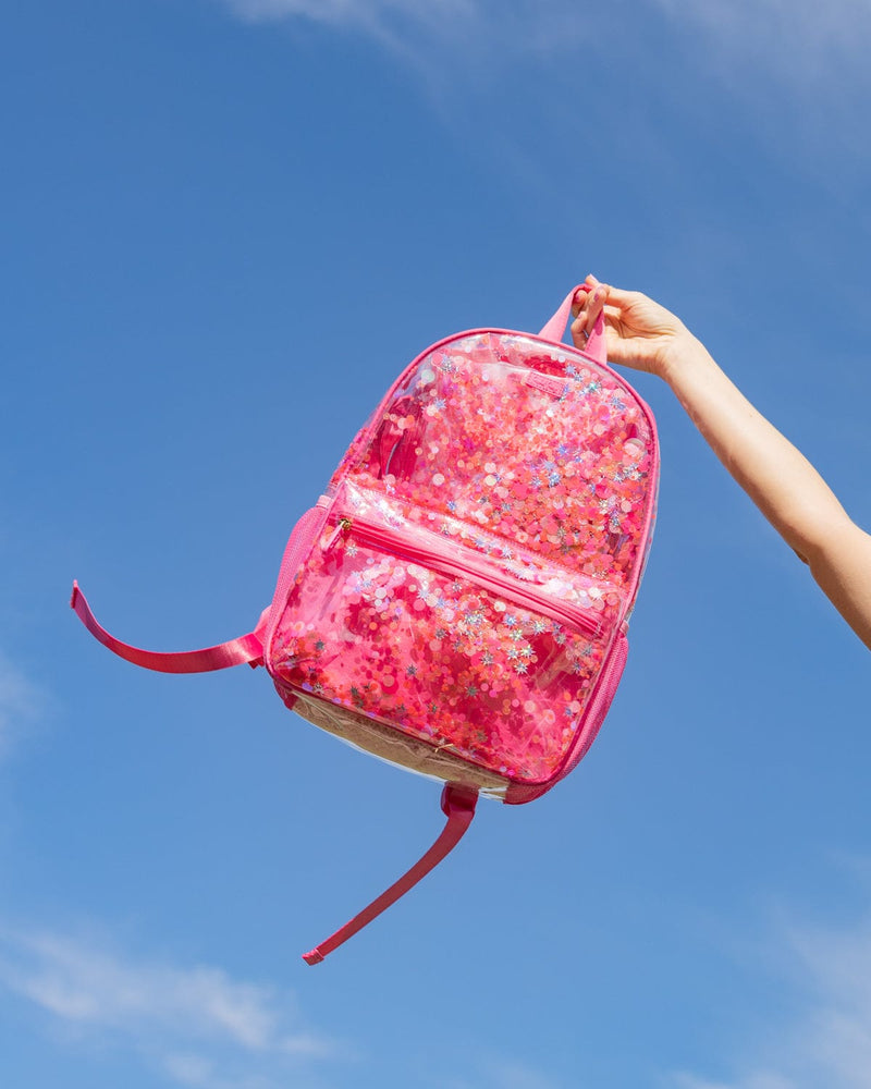 A person holds a pink vinyl backpack with confetti up in the sky. 