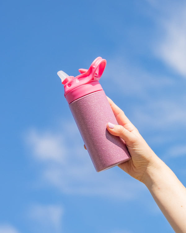 A person holds a pink glittery water bottle with a solid pink pop up lid and handle up to the sky.