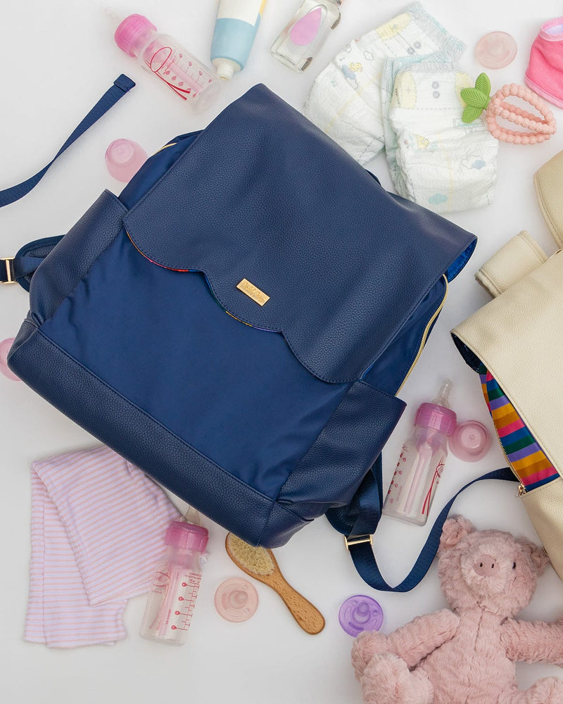 Navy diaper bag backpack surrounded by diapers, baby bottles, teddy bear, and other baby accessories