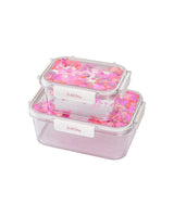 Two lunchboxes with pink confetti trapped inside the flip-top lids sit on top of eachother. One is visible smaller than the other and is sitting on top. 