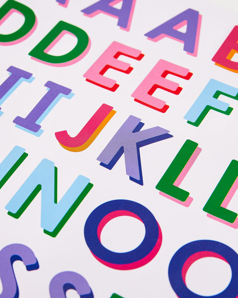 Close up view of some of the multi-colored letters on the sticker sheet. "J" in pink and "K" in purple are most visible. 